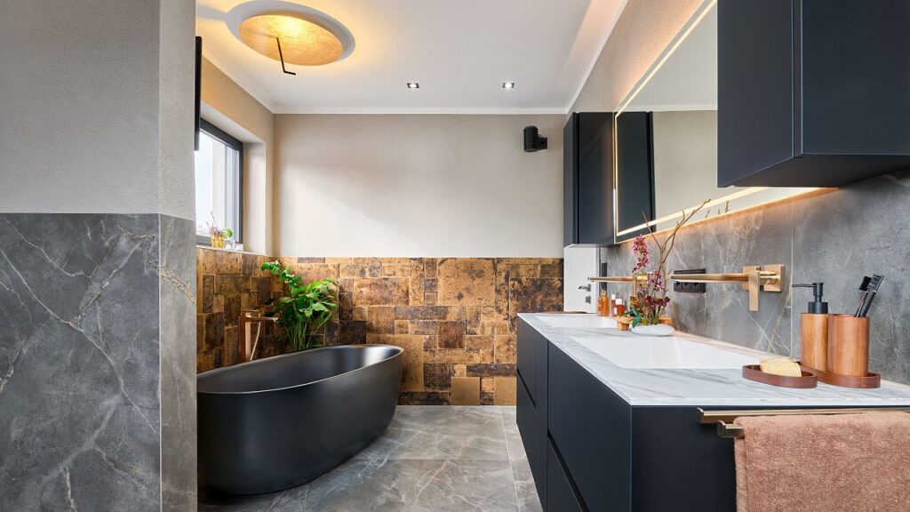 In dem auf Wunsch des Bauherrn offen gestalteten Badezimmer schirmen Raumteiler WC und Urinal sowie gegenüber die bodenebene Dusche mit Regenbrause ab; ein höher gesetztes Fenster bringt Tageslicht und schützt zugleich vor Einblicken. Bild: MHK Group